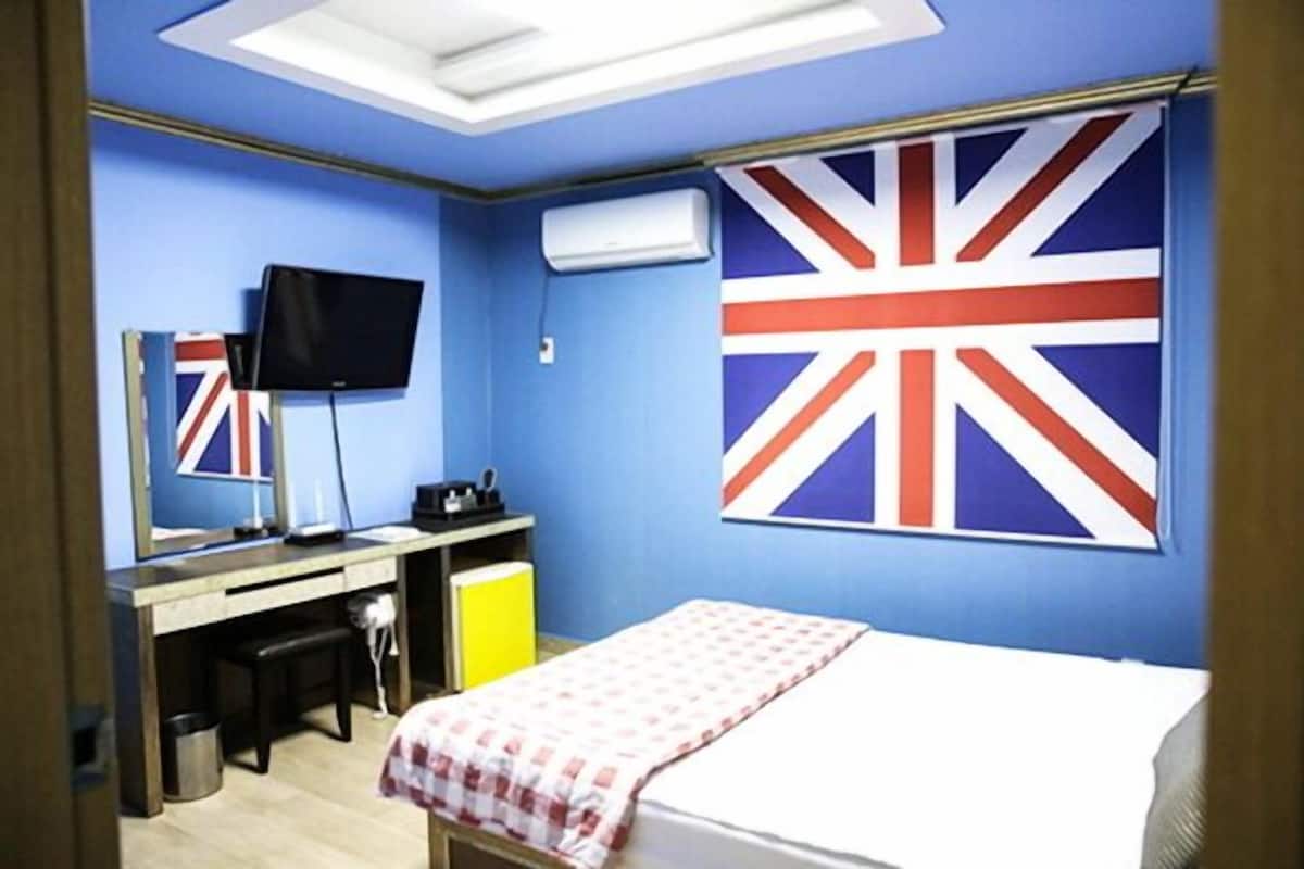 Een kamer met een bed, een bureau, een stoel, een televisie en een grote vlag aan de muur.