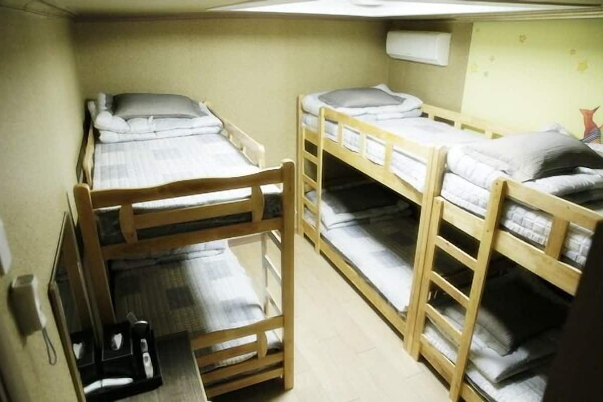 Een slaapzaal met stapelbedden, een klein bureau en een luchtverkoeler aan de muur.