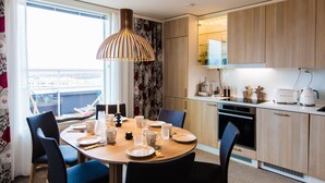 A modern kitchen with wooden cabinets, a dining table set with plates and cups, and a large window with curtains.