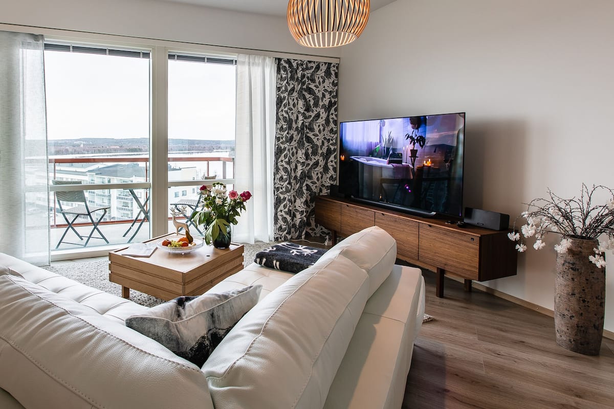 A modern living room with a sofa, coffee table, TV, and a large window with a view.