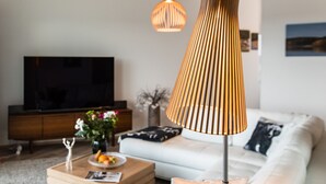 A modern living room with a large flat-screen TV, a wooden coffee table with a magazine, a vase with flowers, and a stylish floor lamp.