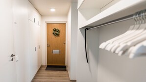 A hallway with a wooden door, a black mat at the entrance, and a clothes rack with hanging clothes.