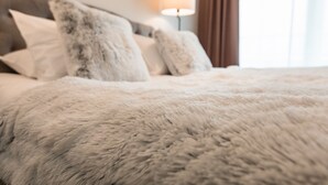 A bed with fluffy white bedding and a lamp in the background.