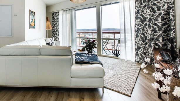 A modern living room with a sofa, large windows, and a view of the city.