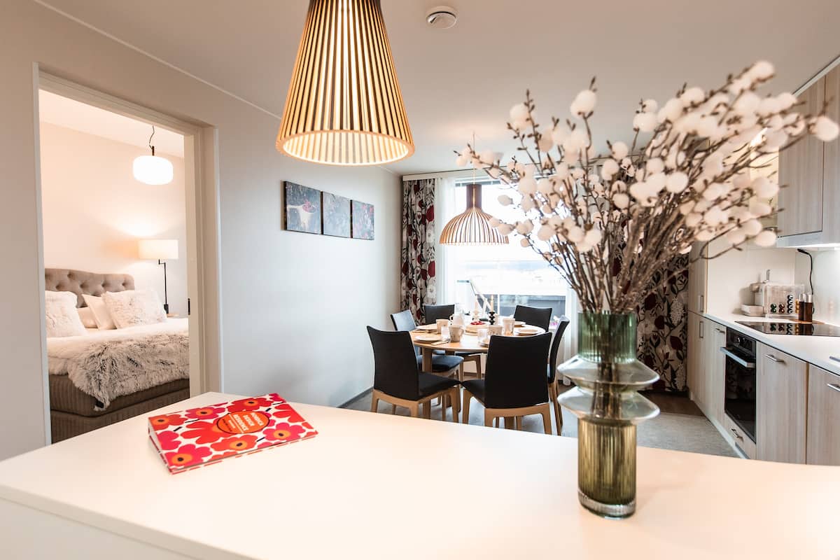 A modern kitchen with a dining area, a white countertop, and a vase with flowers.