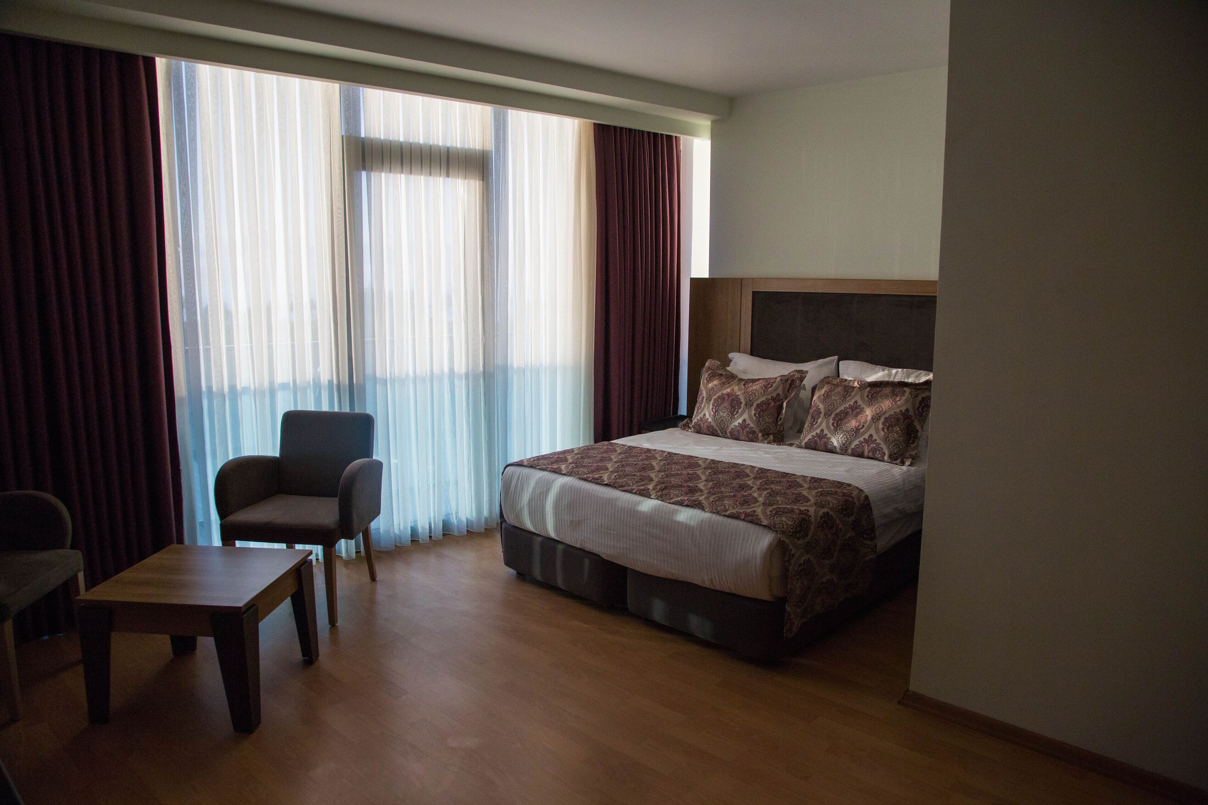 Une chambre d’hôtel avec un lit, une chaise, une petite table et une grande fenêtre avec des rideaux.
