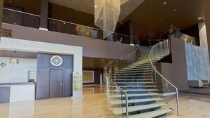 Un lobby moderno de hotel con una escalera de cristal, un mostrador de recepción y una lámpara decorativa.