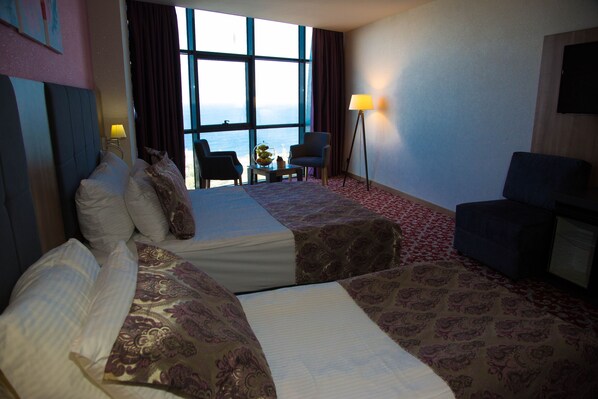 A hotel room with two beds, a desk, a chair, a lamp, and a view of the sea. - Euphoria Hotel Batumi (Batumi)
