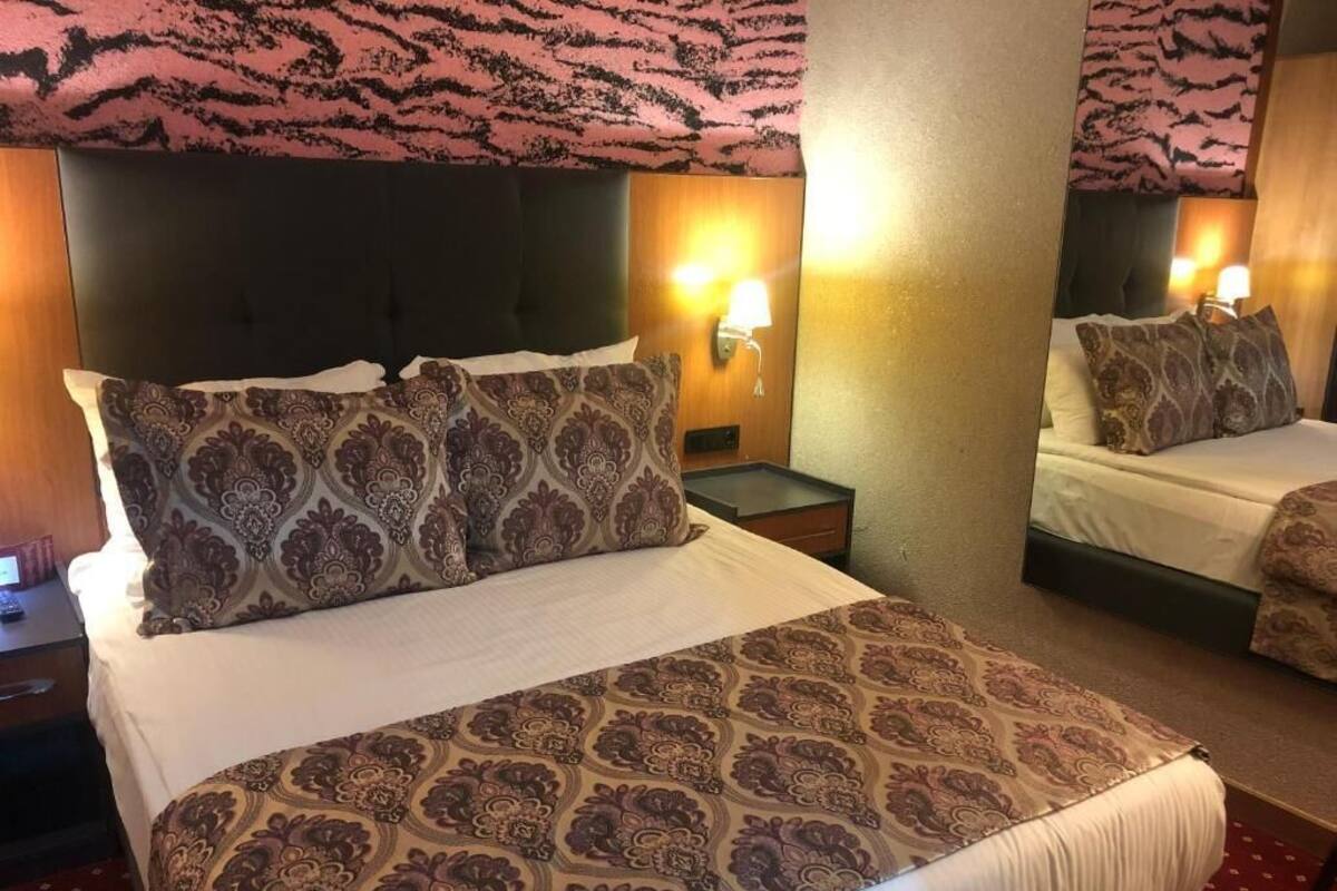 Habitación de hotel con dos camas, cubrecamas estampados, lámparas de noche y cabecera con diseño decorativo.