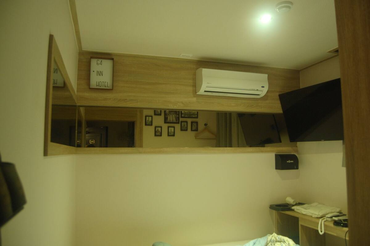 A hotel room with a large mirror, an air conditioner, a desk with a telephone, and a small shelf with items.