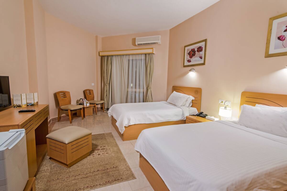 Une chambre d’hôtel avec deux lits, un bureau, une chaise, une petite table et un appareil de climatisation.