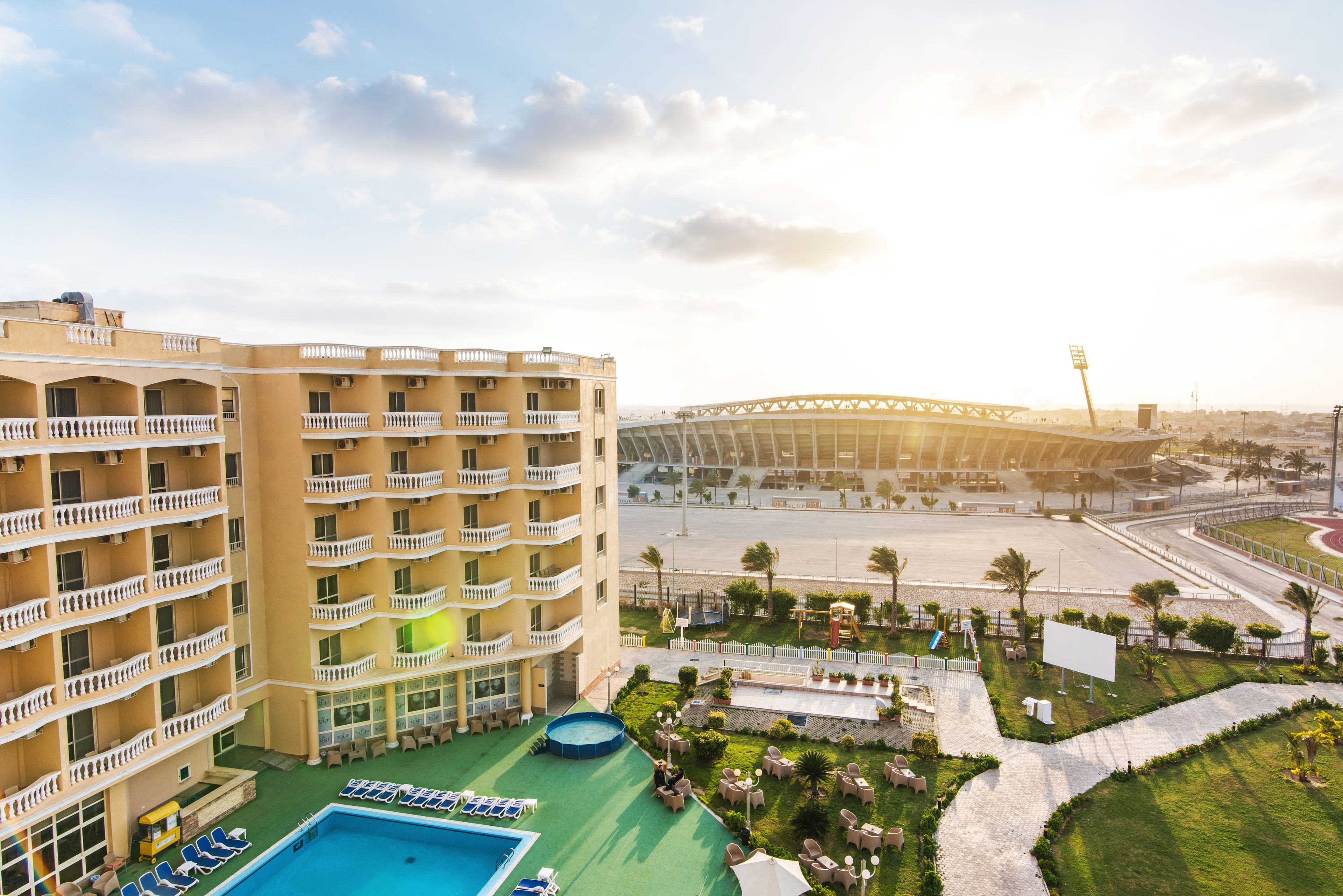 A hotel with multiple balconies, a swimming pool, and a view of a stadium.