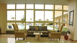 Een hotellobby met een groot raam, een bank, twee fauteuils, een bijzettafeltje en een potplant.