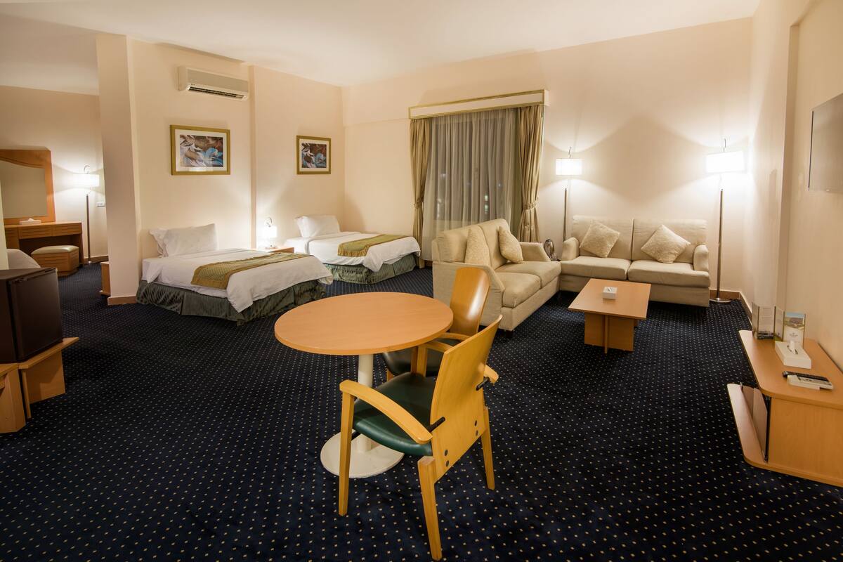 Une chambre d’hôtel comprenant un lit, deux tables de chevet, un canapé, une chaise, une petite table et un téléviseur.