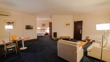 Habitación de hotel con cama, sofá, sillón, mesita, lámpara y televisión.
