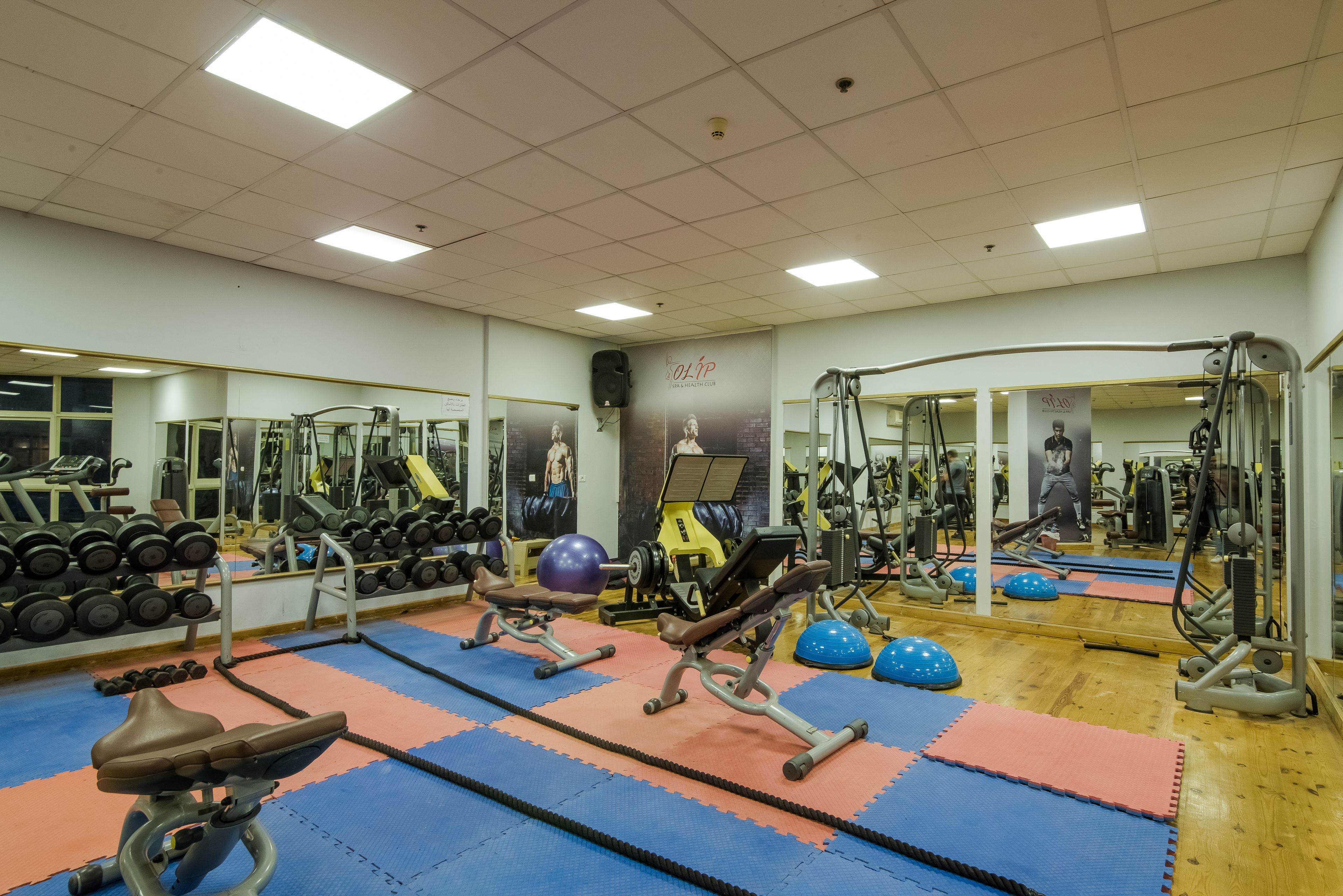 Une salle de sport équipée de matériel d’exercice, de miroirs et d’un mur orné d’affiches.