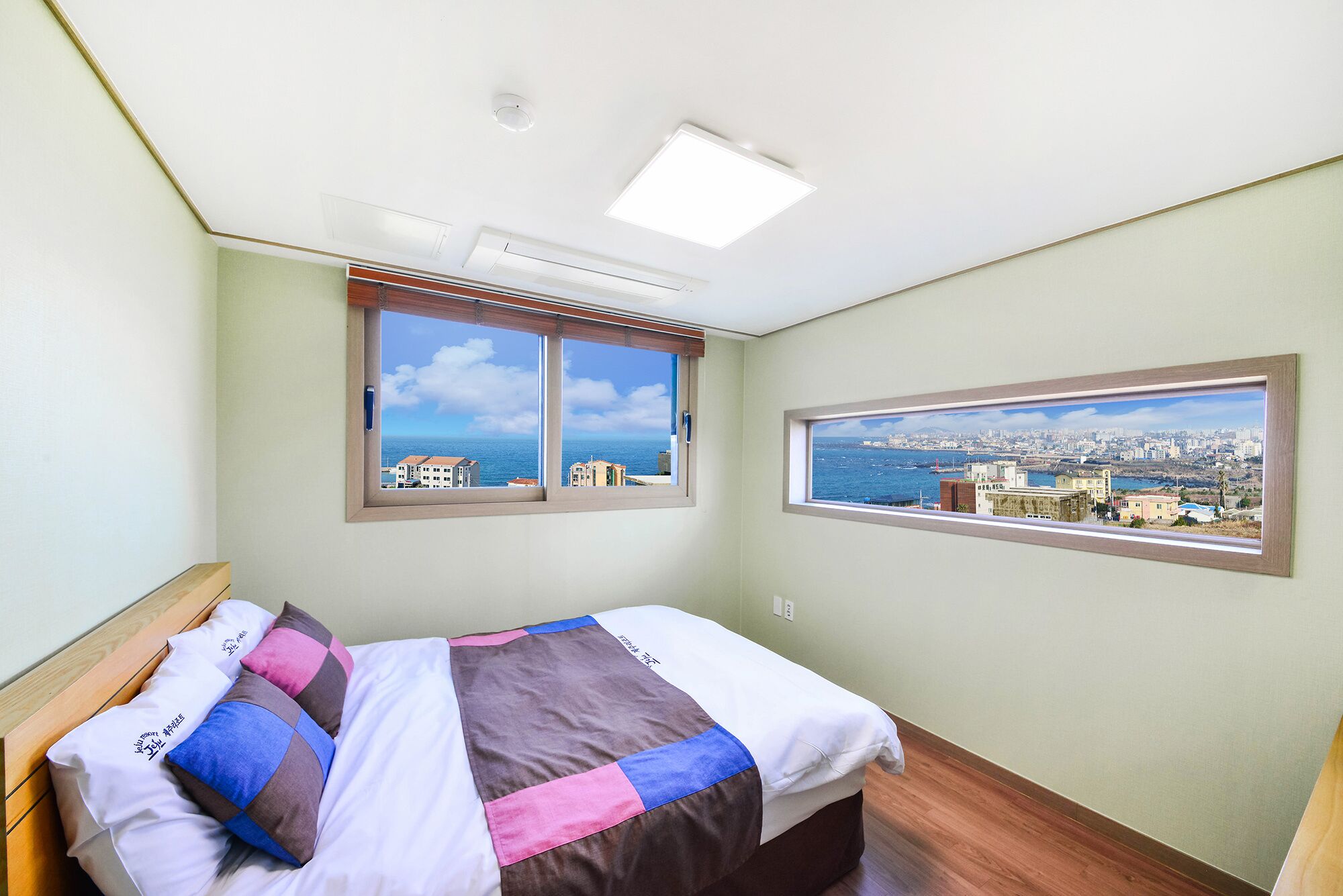 A bedroom with a bed, two windows, and a city view.