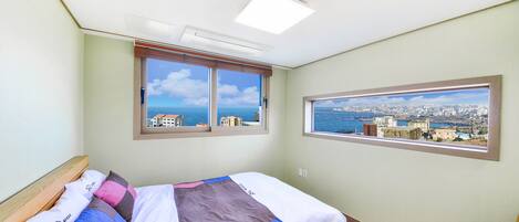 A bedroom with a bed, two windows, and a city view.