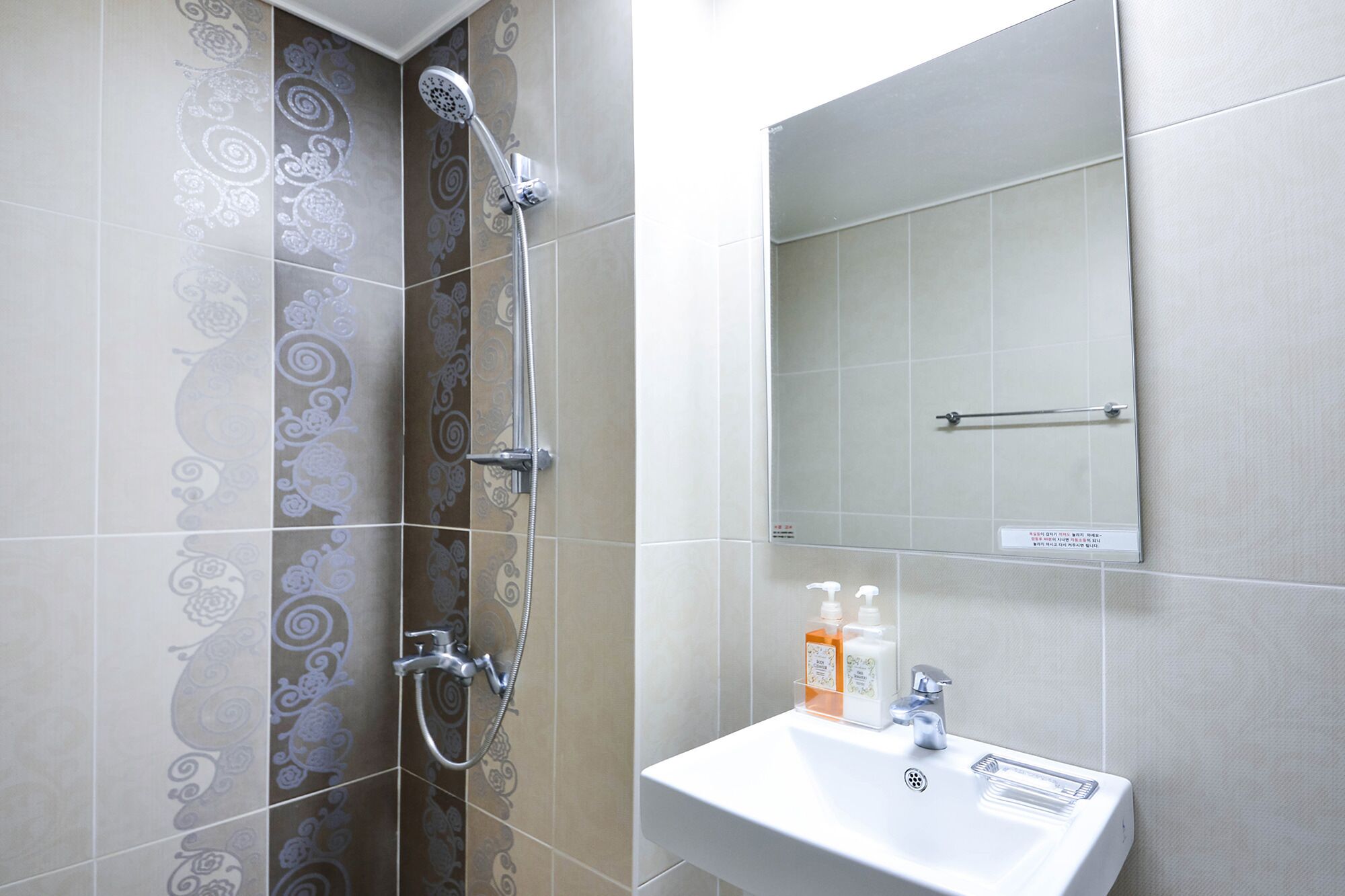 A bathroom with patterned tiles, a shower, a sink with soap dispensers, and a mirror.