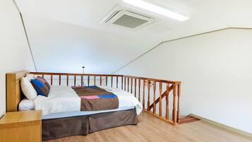 Un dormitorio con cama de madera, paredes blancas, barandilla de madera y techo inclinado con una rejilla.