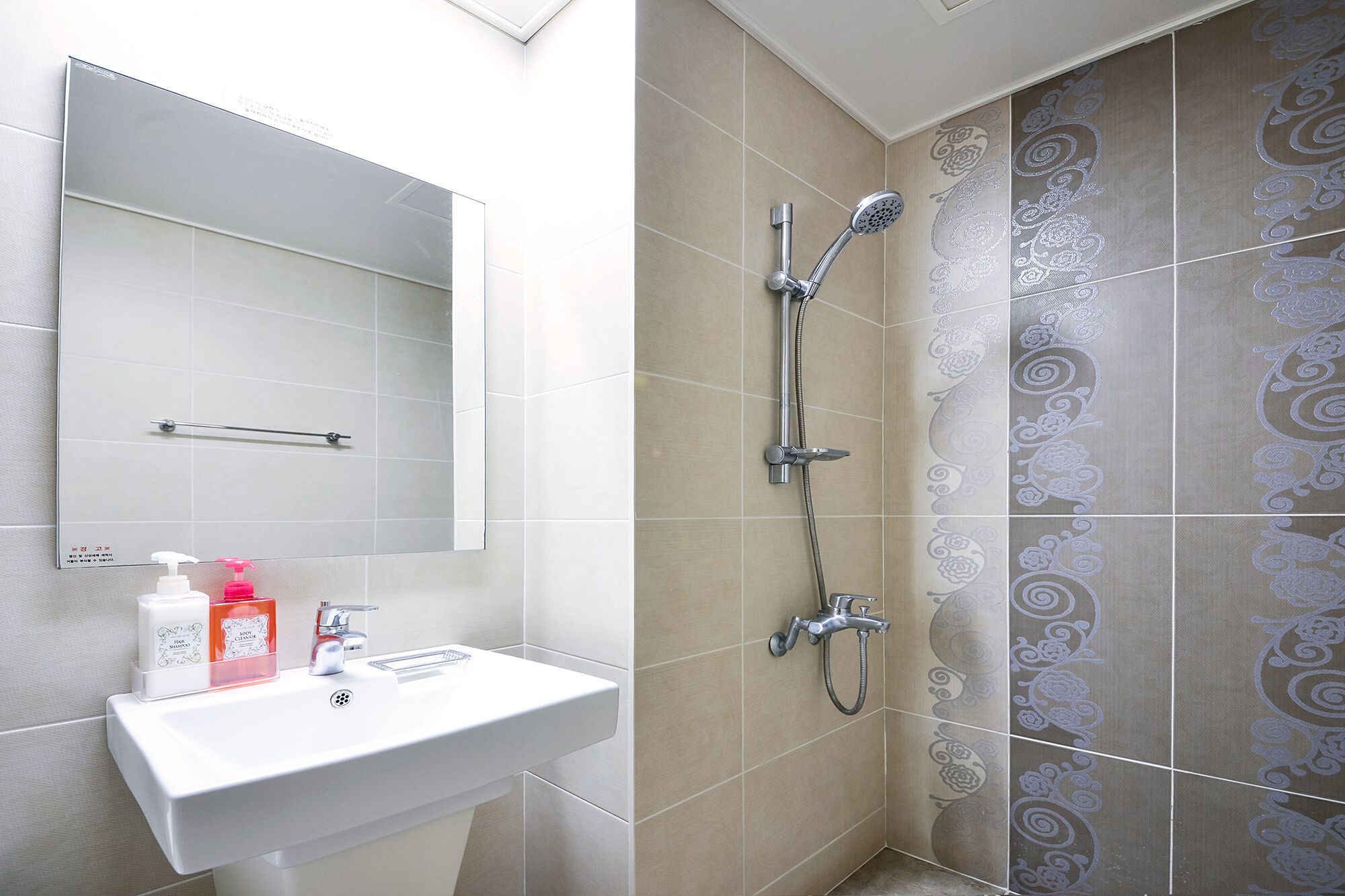 A bathroom with a white sink, a mirror, and a shower with a patterned tile wall.