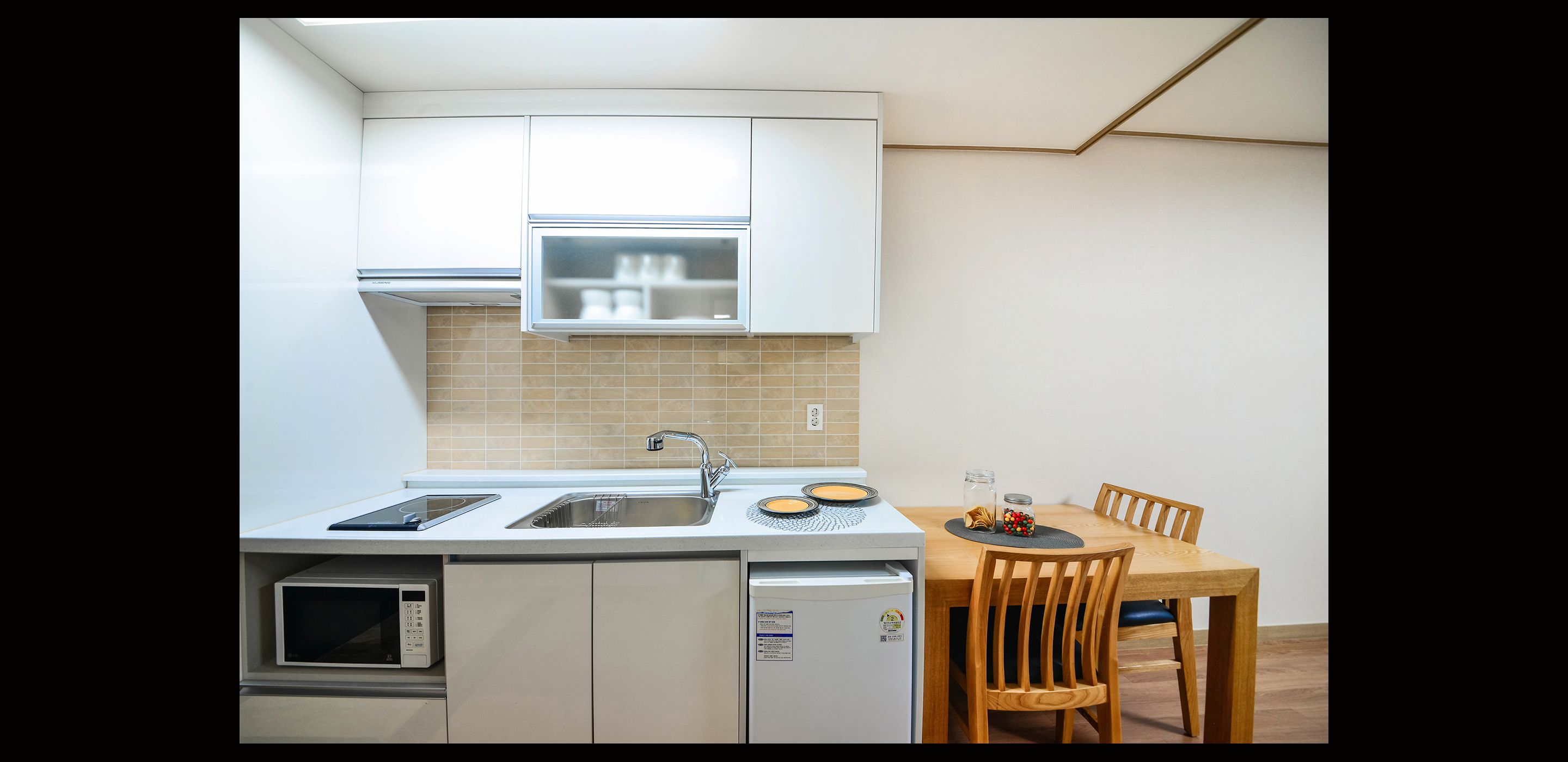A compact kitchen with a built-in microwave, oven, and dishwasher, a small window, and a dining area with a table and chairs.