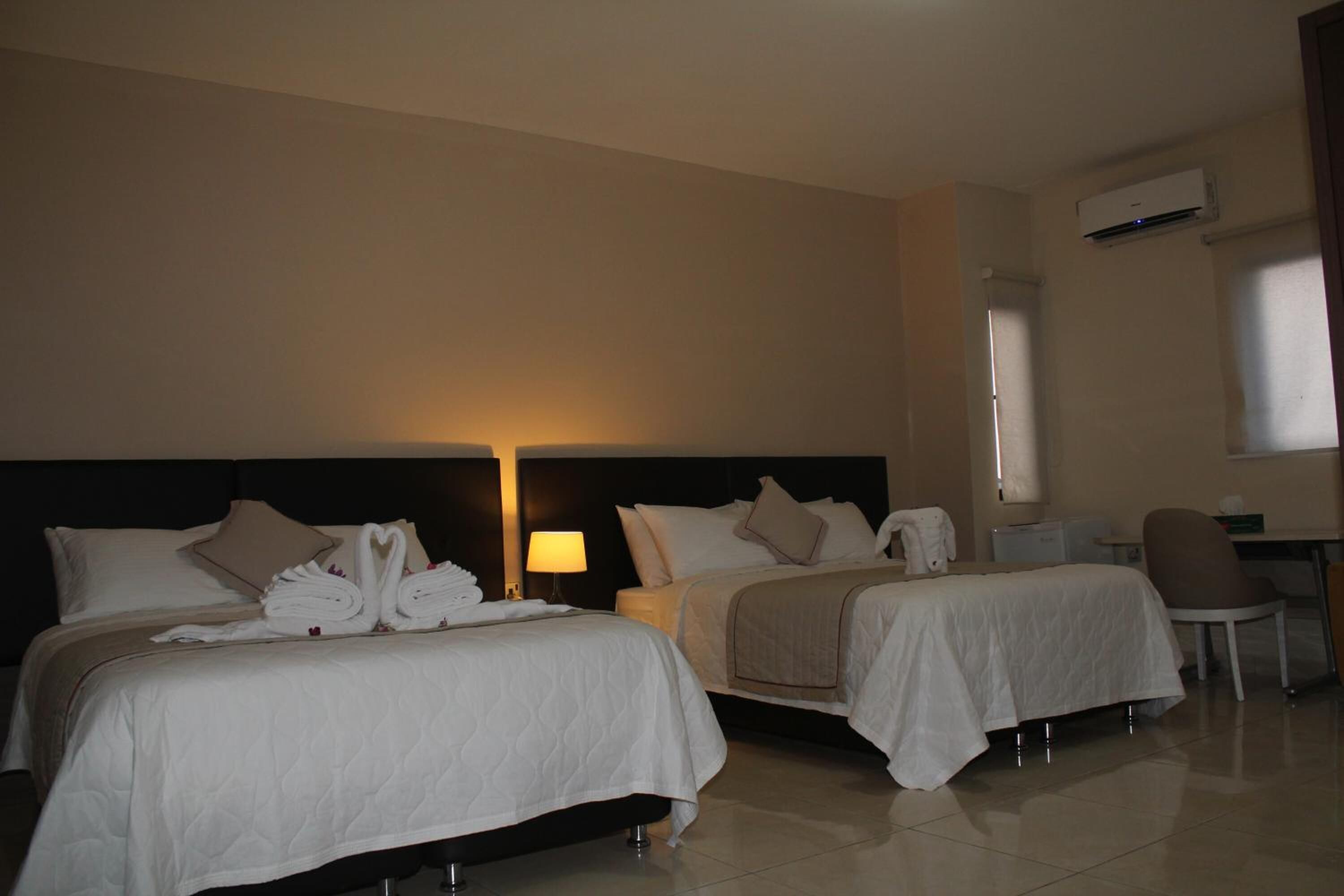 A hotel room with two beds, a desk, a chair, and a lamp.