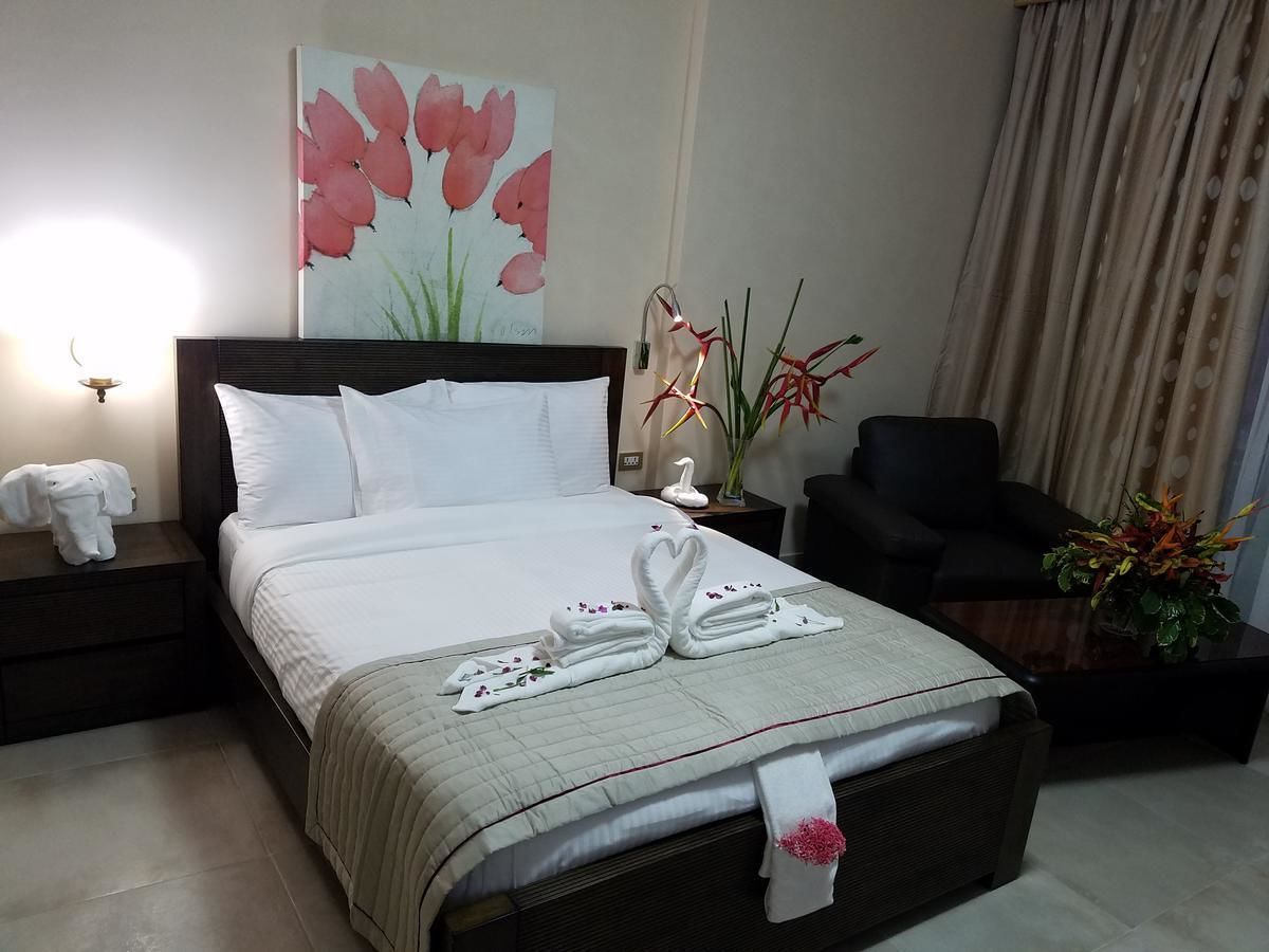 Una cama bien hecha con sábanas blancas y toallas decorativas con forma de cisne, un cuadro de tulipanes rosados en la pared y una silla en la esquina.