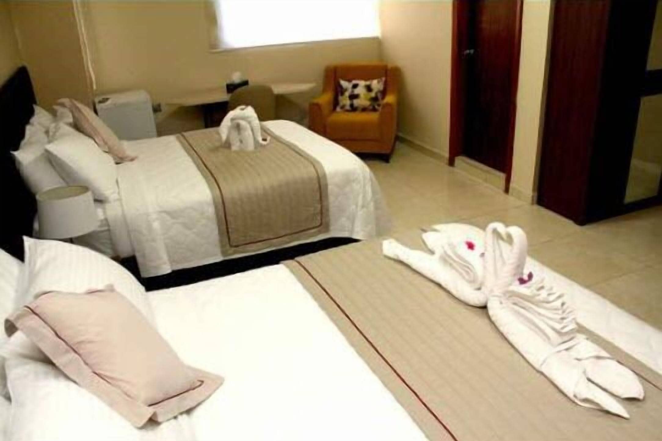 Habitación de hotel con dos camas, una silla y una toalla ordenada en el suelo.