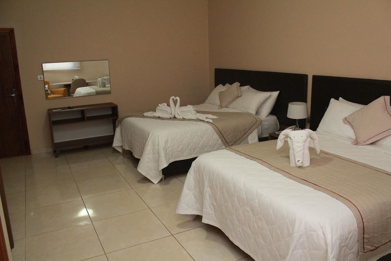 Habitación de hotel con dos camas, una mesita de noche, una lámpara y un espejo.