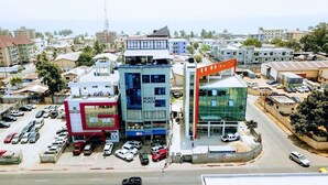 A hotel with a modern glass facade, a red and white building adjacent to it, and a parking lot with several cars. - Murex Plaza Hotel & Suites (Monrovia)