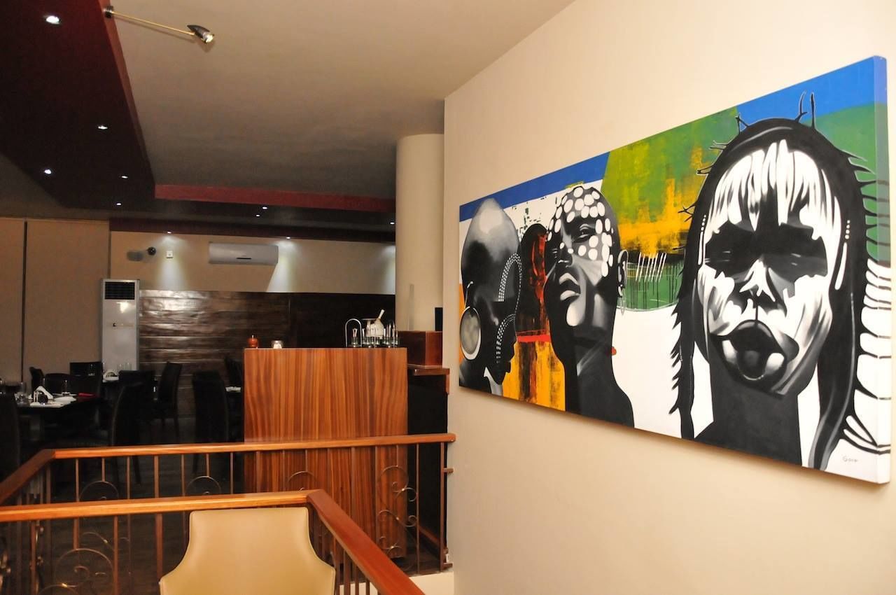 Um saguão moderno de hotel com uma grande pintura abstrata na parede, um balcão de recepção de madeira e uma escadaria com corrimão.