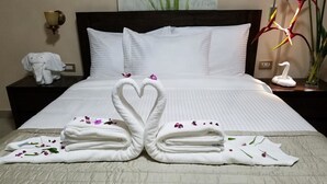 A neatly made bed with two towels arranged in the shape of swans, a nightstand with a lamp, and a vase with a white swan decoration. - Murex Plaza Hotel & Suites (Monrovia)