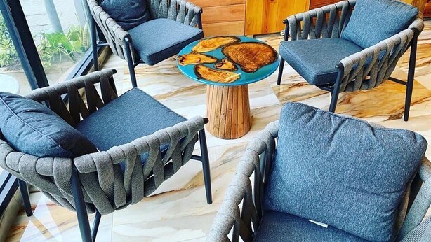 A seating area with four wicker chairs and a round wooden table, featuring a plate of fried plantains. - Murex Plaza Hotel & Suites (Monrovia)
