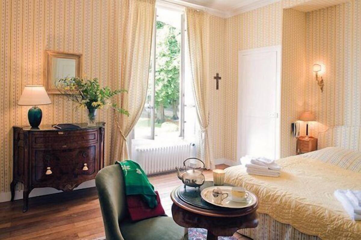 Quarto de hotel com cama, mesa de cabeceira com abajur, cômoda e janela com cortinas.