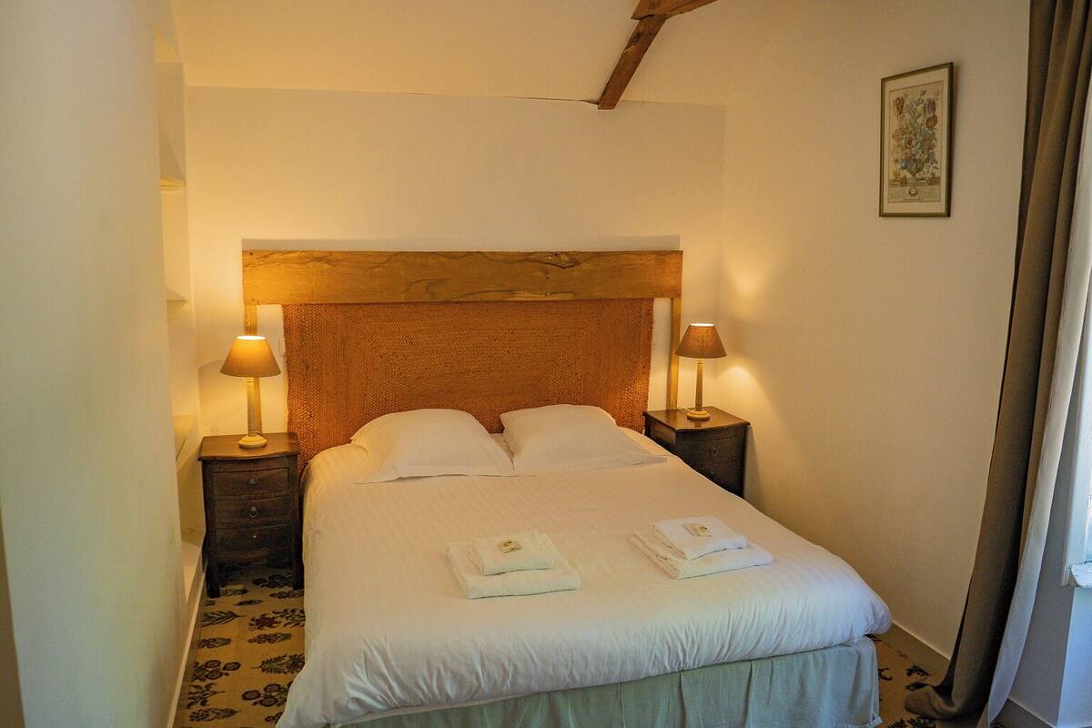 Quarto de hotel com uma cama grande, duas mesas de cabeceira com abajures, uma cabeceira de madeira e um quadro emoldurado na parede.