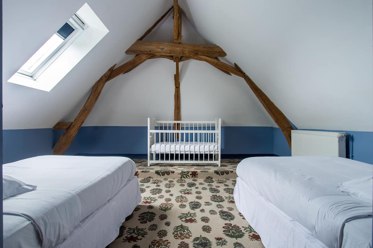 Quarto com teto inclinado, berço, duas camas e um tapete estampado.