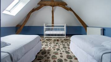 A room with a sloped ceiling, a crib, two beds, and a patterned carpet.
