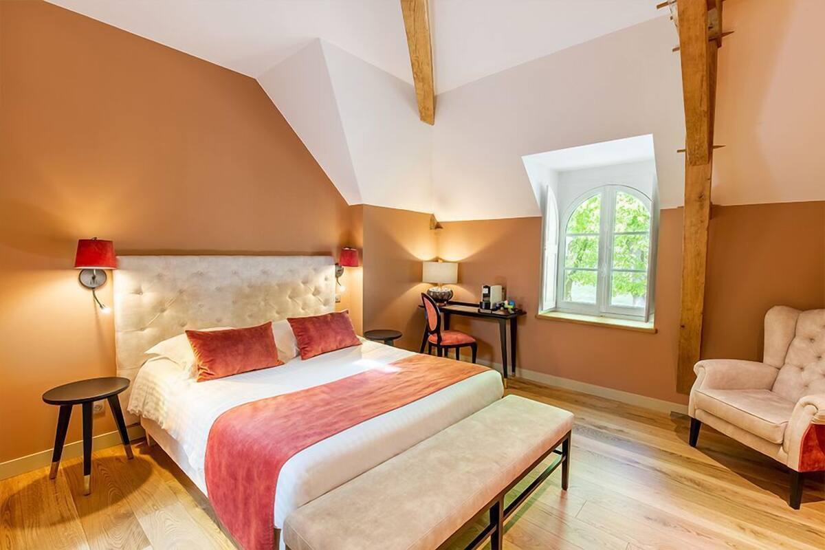 Quarto com uma cama grande, uma escrivaninha, uma cadeira e janela com vista para o verde.