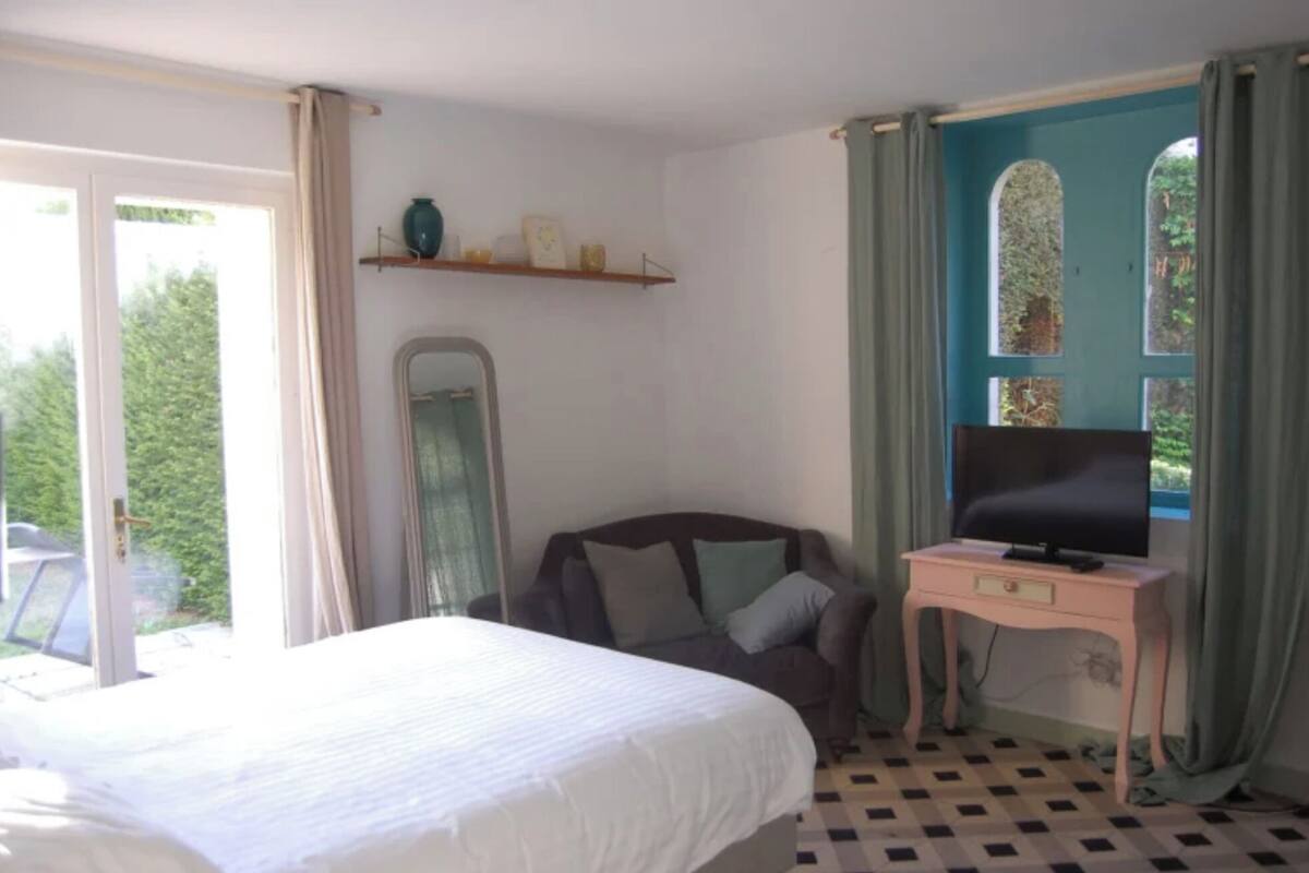 Quarto com cama, televisão em móvel, espelho e janela com cortinas.