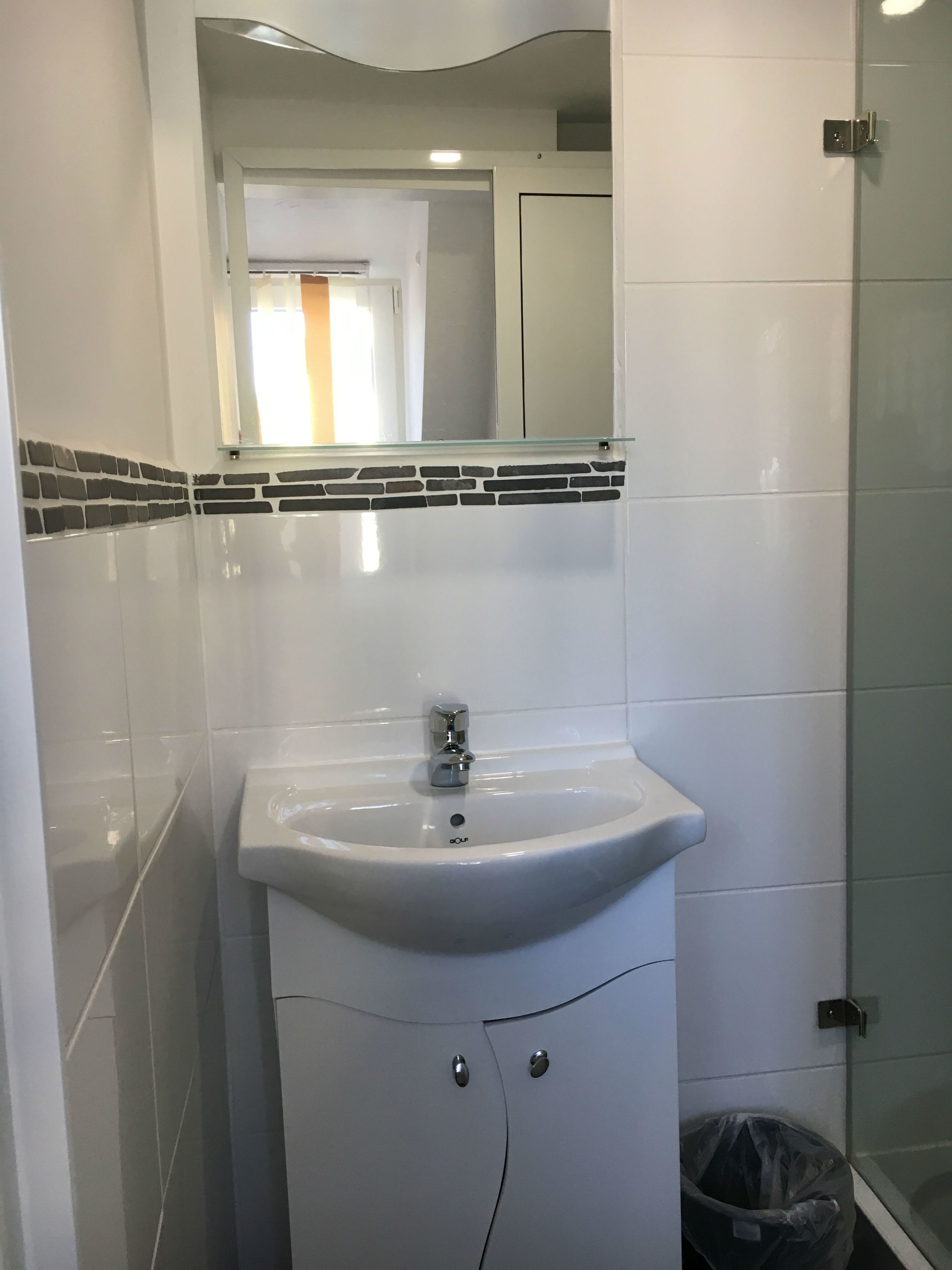 A bathroom with a white sink, a mirror above it, and a glass shower door.