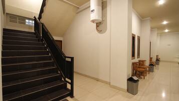 A staircase with black railings leading to a landing. A white cylindrical object is mounted on the wall above the stairs.