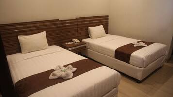 A hotel room with two single beds, each with a wooden headboard, white bedding, and a brown accent on the bedspread. There is a bedside table with a phone and a small lamp.