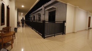 A spacious corridor with wooden chairs, a black railing, and a person walking. - Palapa Hotel (Mataram)