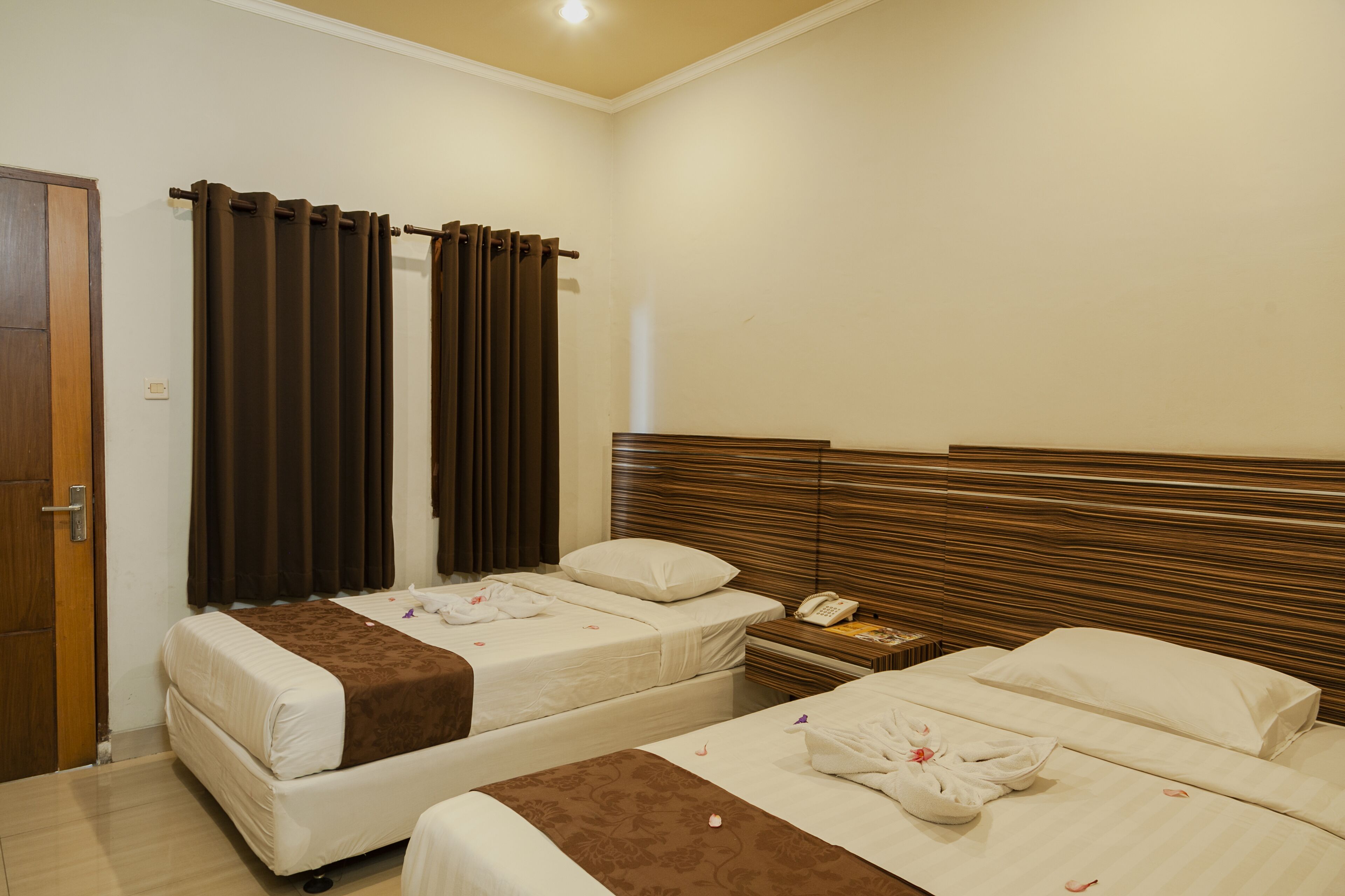 Quarto de hotel com duas camas, cabeceira de madeira, mesa de cabeceira e uma porta.