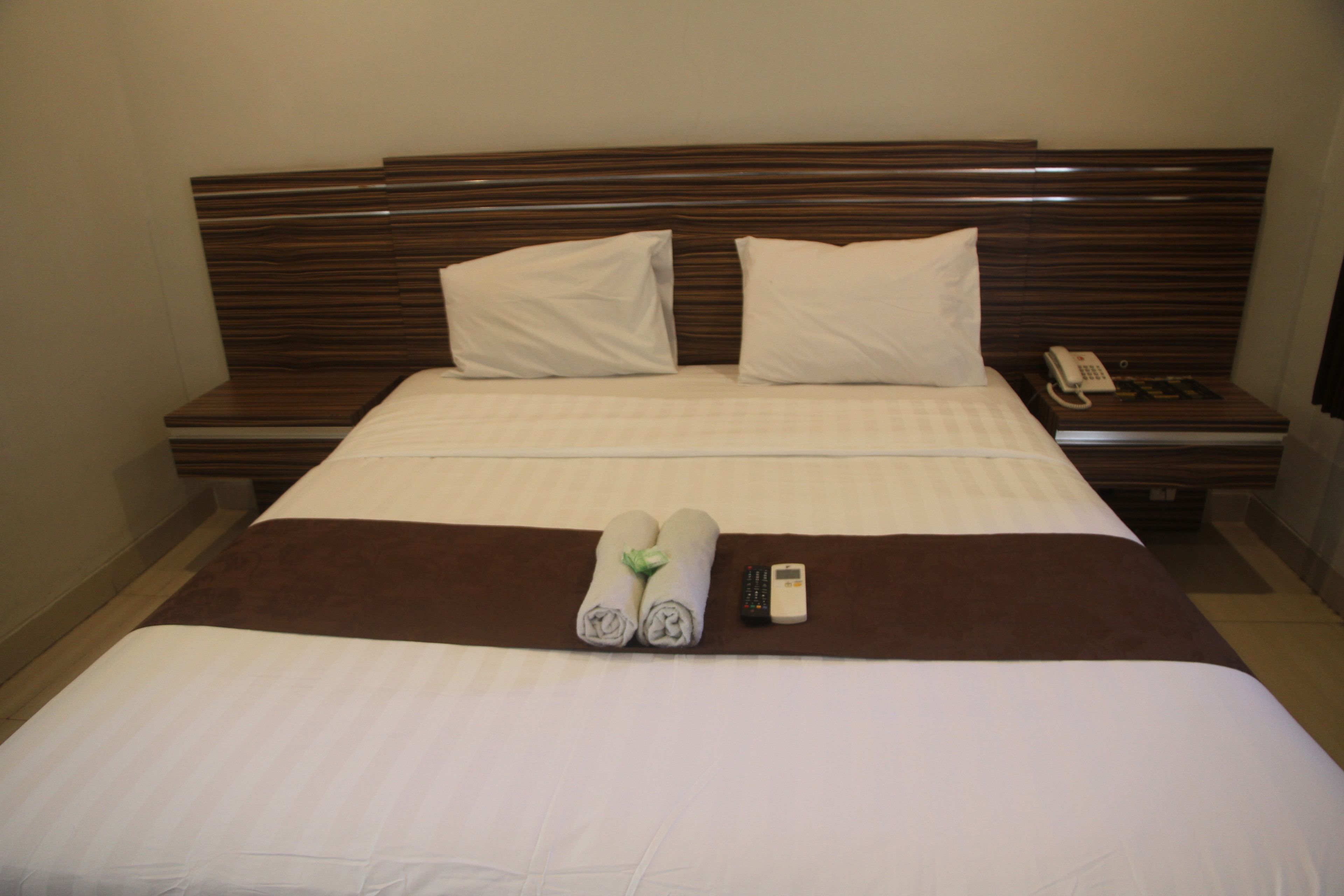A neatly made bed with white linens, two pillows, a brown bedspread, and a remote control on the side.