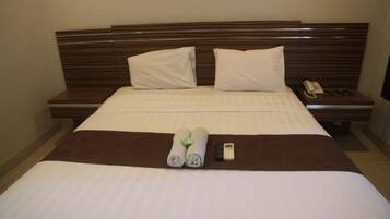 A neatly made bed with white linens, two pillows, a brown bedspread, and a remote control on the side.