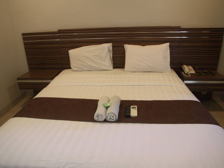 A neatly made bed with white linens, two pillows, a brown bedspread, and a remote control on the side.