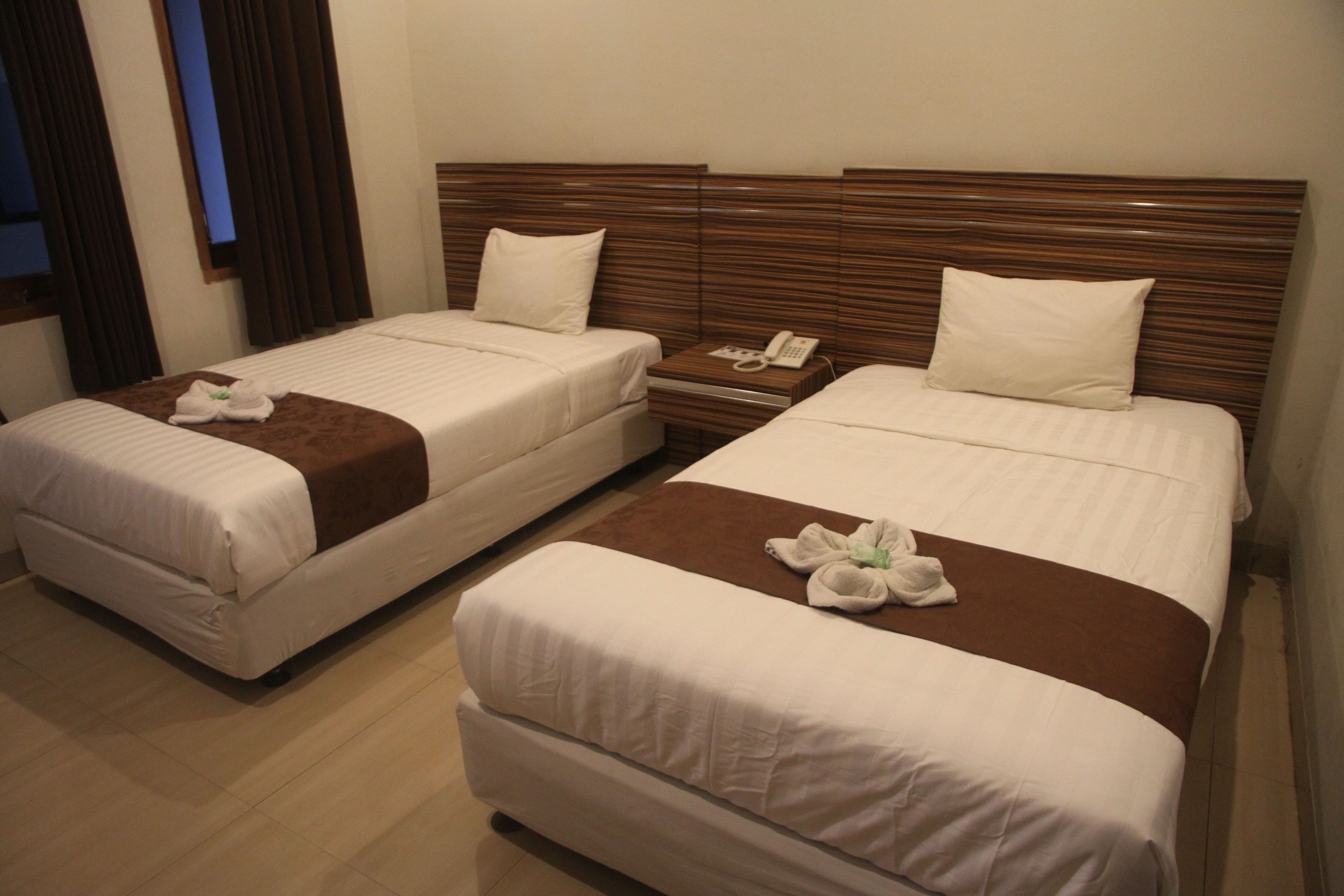Two single beds with wooden headboards, a bedside table with a phone, and a brown accent pillow.