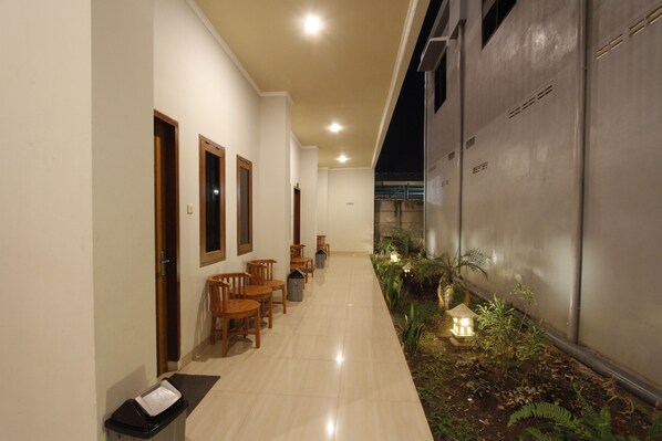 A hallway with wooden chairs and tables, a trash bin, and a small garden area with plants and a lantern.